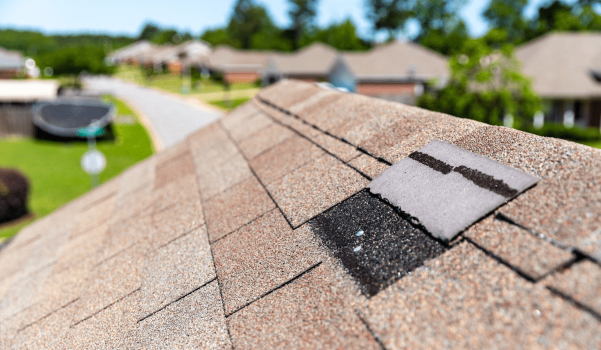 Close-up of folded shingle below ridge on asphalt roof under a clear sky—highlighting signs of roof damage in need of professional repair