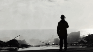 Silhouette of firefighter on roof of destroyed Pacific Palisades home after recent wildfire