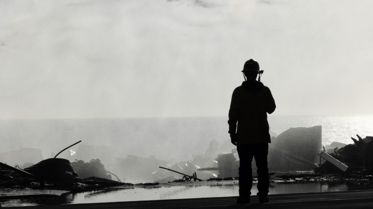 Silhouette of firefighter on roof of destroyed Pacific Palisades home after recent wildfire