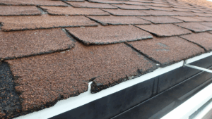 Close-up of cracked and curling asphalt shingles, showing age-related roof damage that increases fire vulnerability