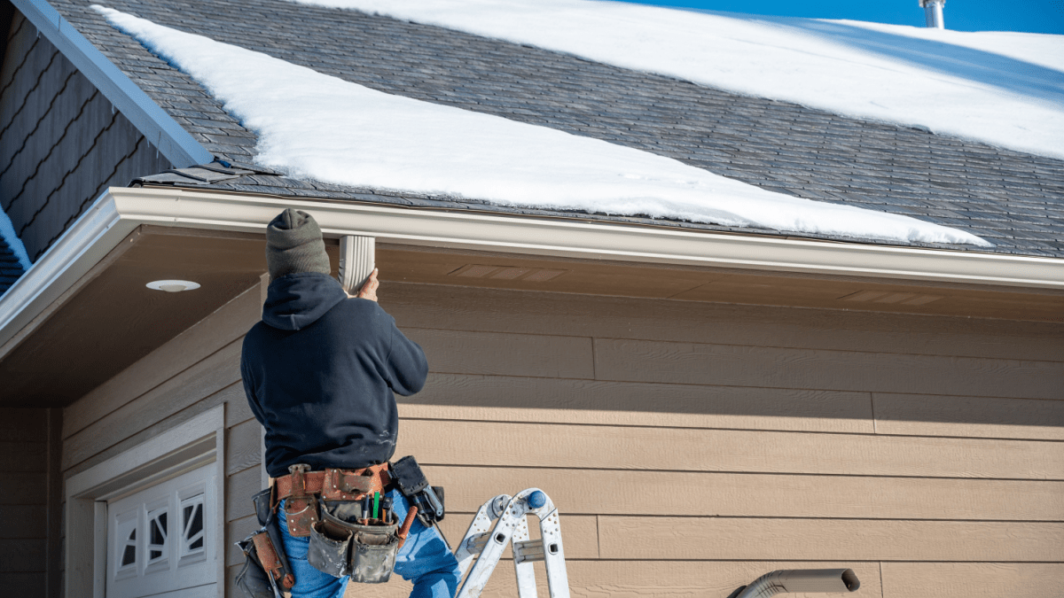 Man on ladder inspecting snow-covered roof in Tehachapi—highlighting key steps for winter roof preparation in cold mountain climates