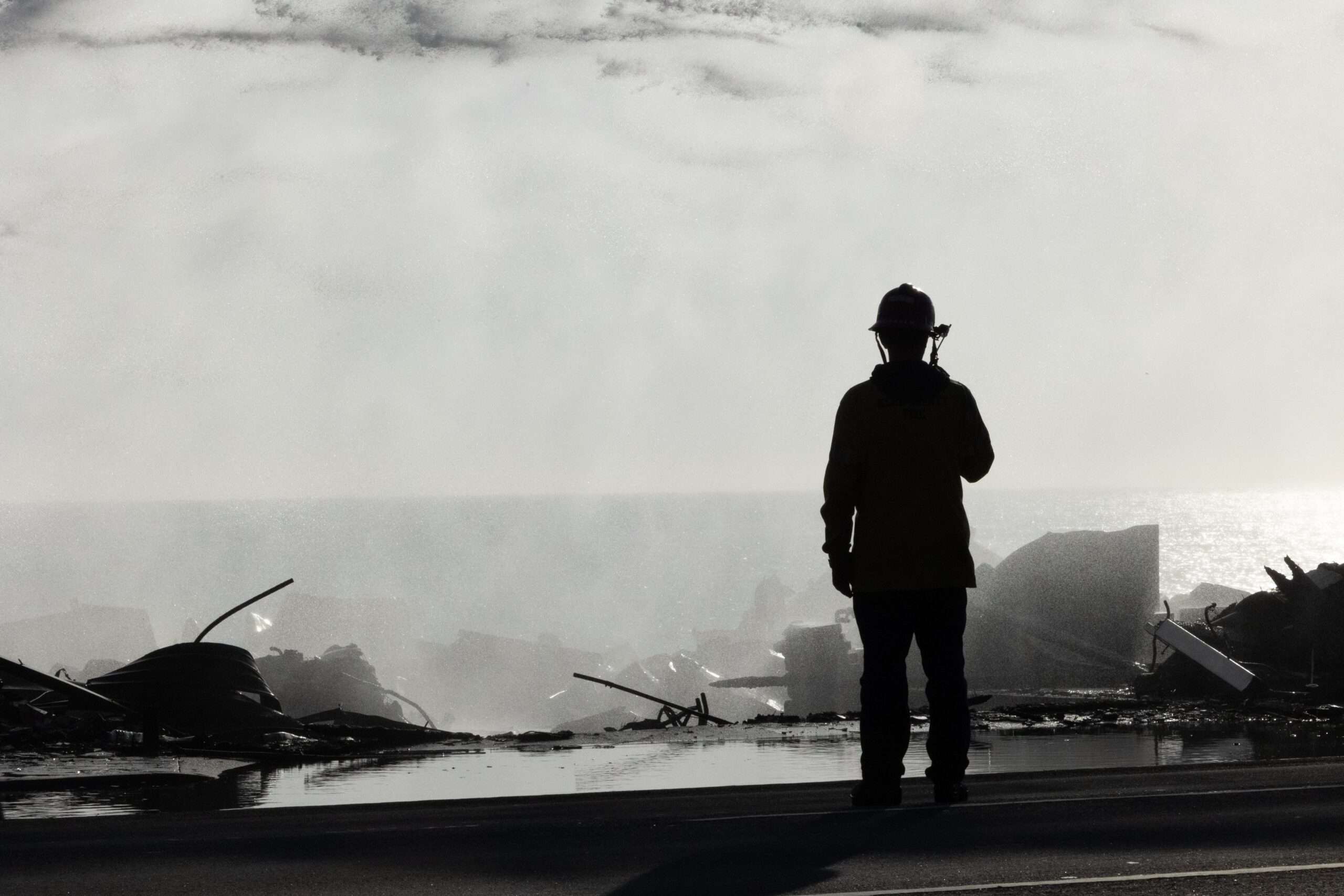 Silhouette of firefighter on roof of destroyed Pacific Palisades home after recent wildfire