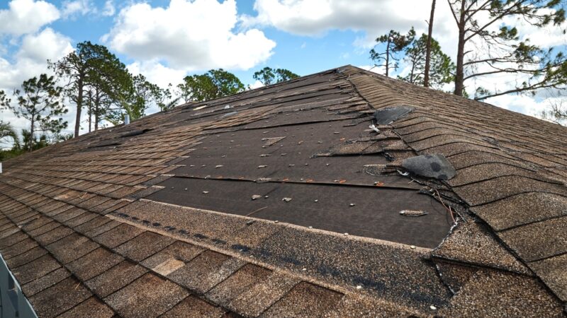 Damaged asphalt shingle roof with missing shingles and exposed underlayment, showing need for roof replacement
